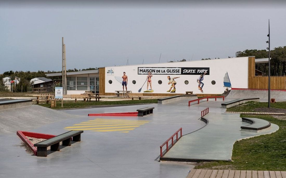 La Maison de la Glisse : un bâtiment blanc bardé de bois, l'enseigne « Maison de la Glisse – Skate park » sur la façade, le skatepark devant