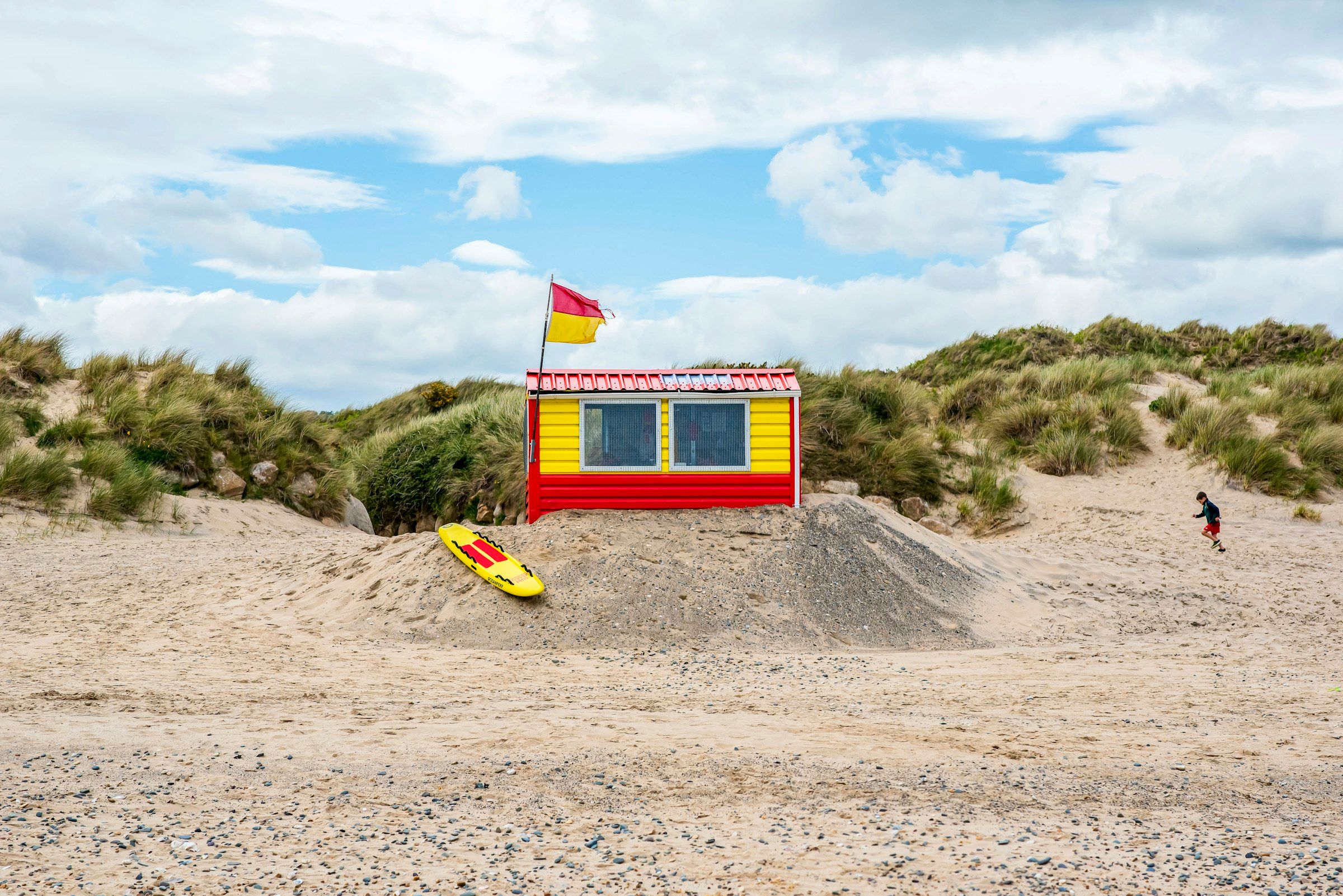 Un poste de secours rouge et jaune au pied des dunes, drapeau de baignade hissé